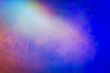 Extreme close up of abstract vibrant iridescent holographic rainbow foil background with lens flare. Glitter surface. Selective soft focus, shallow depth of field. © Taigi