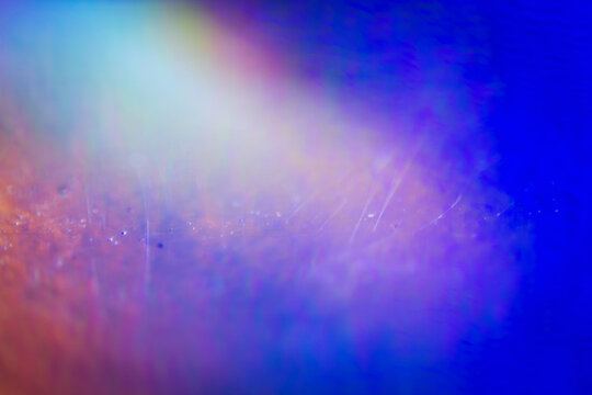 Extreme close up of abstract vibrant iridescent holographic rainbow foil background with lens flare. Glitter surface. Selective soft focus, shallow depth of field.