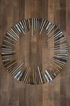 Circle made of various screws and nails on brown wood texture. Industrial flat lay. Carpentry still life.