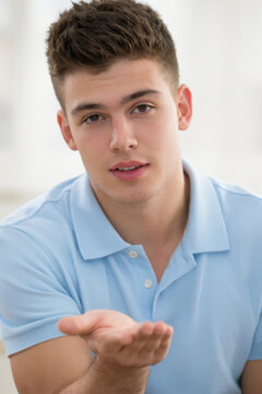 A young handsome guy in a blue polo shirt shows an open palm, you can insert the advertised item.