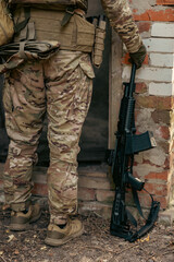 Obraz premium A soldier's legs next to an assault rifle. The soldier stands near the entrance to a ruined building
