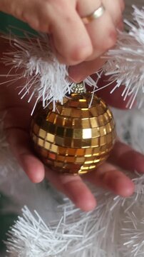 Vertical video. Hands hanging on Christmas tree golden bauble