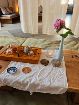 A traditional Chinese tea ceremony table setting featuring a wooden gongfu tea tray, glass server, ceramic teapot, lit candle, and a pink hydrangea flower in a tall blue vase.