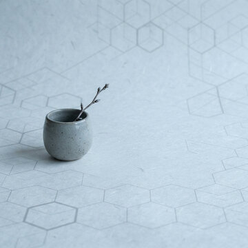 Speckled grey ceramic cup holding a budding twig on a hexagon backdrop