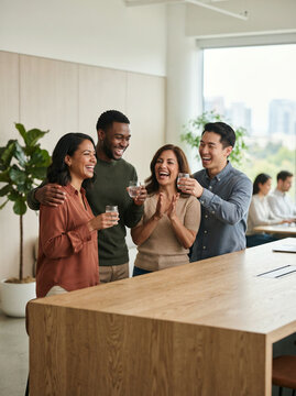 Four colleagues with glass cups chatting by a table in a workspace in soft natural light