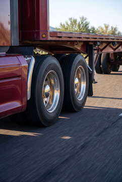 Red semi truck driving on highway, close up of wheels and flatbed trailer on the road