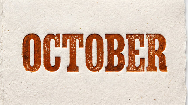 Textured typography reading October in bold brown letters stamped onto a cream handmade paper background