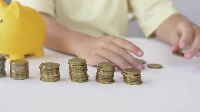 Two hands arrange coin stacks together near yellow piggy bank edge on table on wooden table. Family budget planning shows shared responsibility teaching children steady saving habits early 