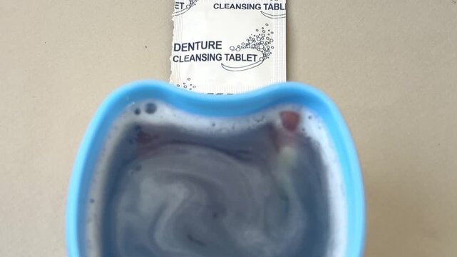 Denture cleaning tablet dissolving in blue container of water  