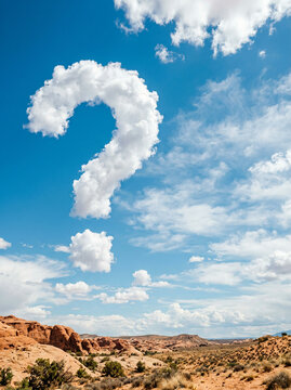 White cumulus clouds forming a question mark over red desert rock in soft daylight