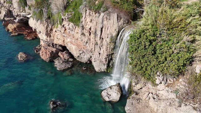 High-angle shot featuring fresh water cascading off steep rocky cliffs into the clear turquoise Mediterranean Sea