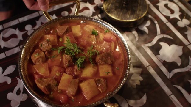 Traditional Turkish stew with meat and potatoes served in a copper pan on patterned table
