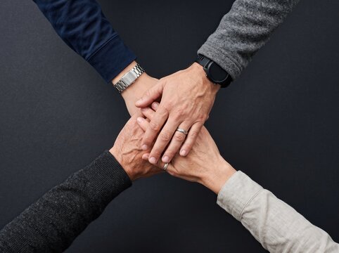 Hands of diverse individuals collaborating in unity on a black background for teamwork concept