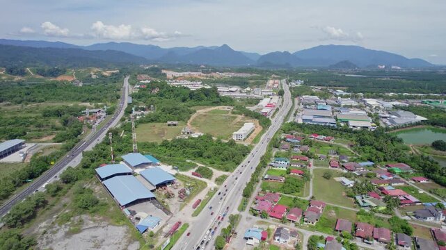 Smooth drone orbit over highways and developing areas in Malaysia, revealing residential neighborhoods, industrial buildings, green countryside and mountains across the horizon.