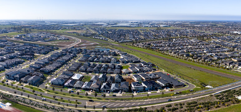 Panoramic high-angle aerial view of expansive layout of modern suburban housing developments,&nbsp;roadways, railway and surrounding open green buffer in Truganina, Melbourne, Victoria, Australia