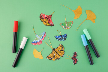 Painted butterflies and ginkgo leaves with markers on green background. Flat lay photography with copy space. Nature art and autumn concept. Design for poster, wallpaper, textile, postcard, © Elena