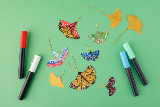 Painted butterflies and ginkgo leaves with markers on green background. Flat lay photography with copy space. Nature art and autumn concept. Design for poster, wallpaper, textile, postcard,