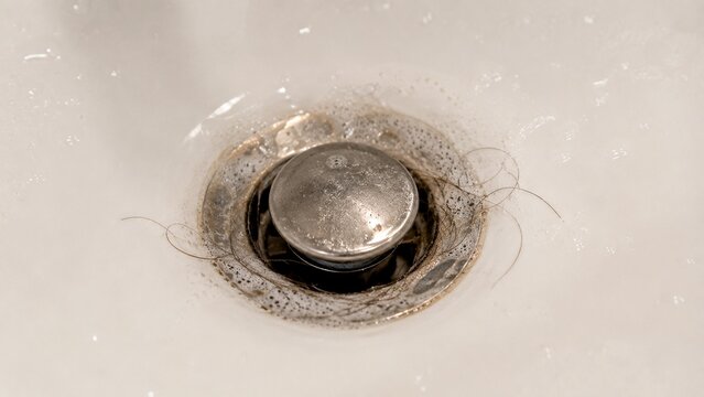 Close-up of bathroom sink drain showing ordinary soap residue and small amount of hair buildup around drain opening associated with slow drainage