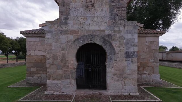 Aerial drone pull-back shot from horseshoe arch porch revealing the 7th-century Visigothic Church of San Juan de Ba&ntilde;os in Palencia, Spain.