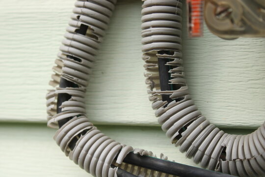Damaged cracked corrugated conduit pipe with exposed electrical wire