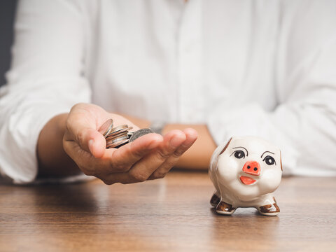 Person holding coins beside piggy bank for saving money