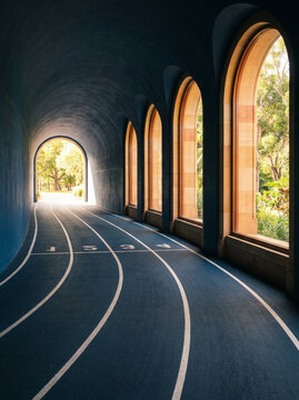 Running track lanes inside a tunnel with arched windows to green space