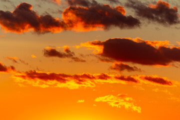Fototapeta premium Fiery orange clouds glowing against a golden sunset sky, dramatic atmospheric light creating a vibrant celestial canvas with intense warm hues during the magical golden hour