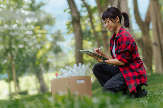 Close-up of a volunteer holding a digital tablet and stylus pen to record plastic bottle recycling data next to a cardboard collection box.