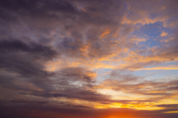 Fototapeta premium Dramatic colorful sunset sky with beautiful clouds,A breathtaking view of a vibrant sunset sky filled with dramatic dark clouds, glowing orange light, and deep purple hues during twilight.