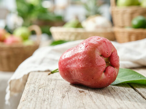 Single pink jambu fruit with a leaf on a weathered wooden surface in daylight