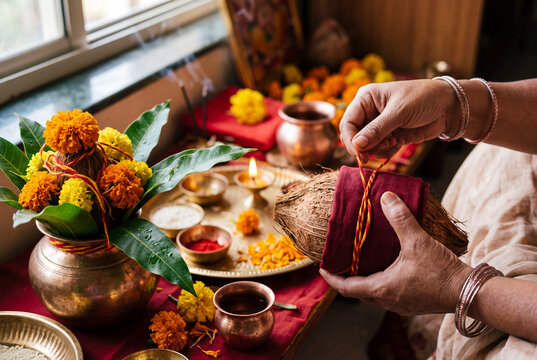 Closeup of hands preparing puja kalash and tying sacred thread with marigold and brass plates for ritual decoration and ceremony detail