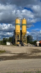 Yellow industrial silos with loader at construction facility under dramatic cloudy sky, outdoor storage tanks and heavy equipment on a modern industrial site © Fluffy