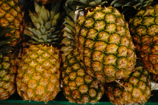 A close-up detailed view of ripe pineapples stacked together showcasing their textured green and yellow skin and leafy crowns
