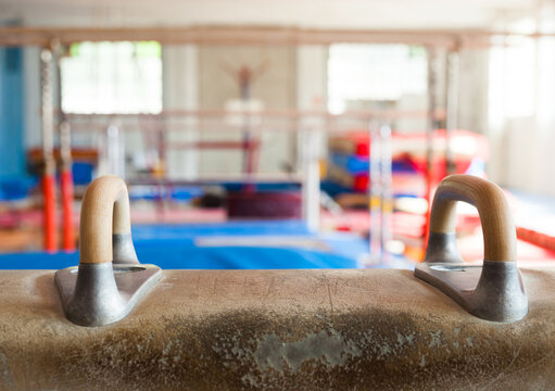 Pommel horse in gymnasium. The horse is tan leather with wooden legs and handles