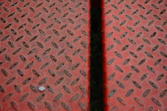Red diamond plate metal surface with a textured weathered and rusted appearance viewed from directly above