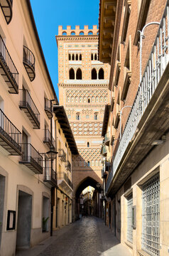 Narrow street leading to San Martin Mudejar tower in Teruel Spain. Historic cobblestone alleyway, traditional buildings and brick tower. High quality photo