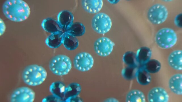 Sparkling cyan rhinestones and turquoise gems rotating with glitter reflections. Abstract craft background with shiny blue flower shaped jewels and iridescent beads