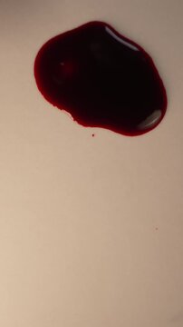 Round blood droplet dripping into pool on neutral background for forensic thriller, top view zoom in slow motion, bottom copy space, vertical video