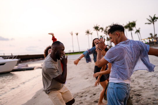 Energetic young people dancing with joy on the sandy beach at sunset, celebrating summer and freedom
