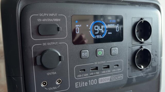 Woman's hand turning on a portable power station, revealing a fully charged battery on the lcd screen, highlighting its renewable energy and off grid power supply capabilities