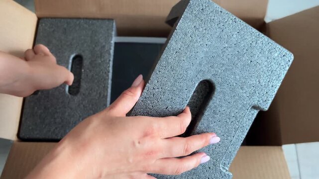 Woman unpacking a new portable power station, removing the electrical generator from its cardboard box and placing the powerful lithium battery on the floor at home