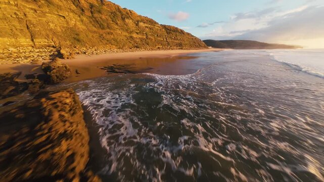 Sunset paints coastal rocks golden. Waves crash against rugged cliffs. Golden light reflects on wet stones. Calm, peaceful, natural beauty. Ideal for travel, nature, or relaxation themes