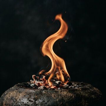 Small fire burning on a rough dark rock against a blurred dark backdrop