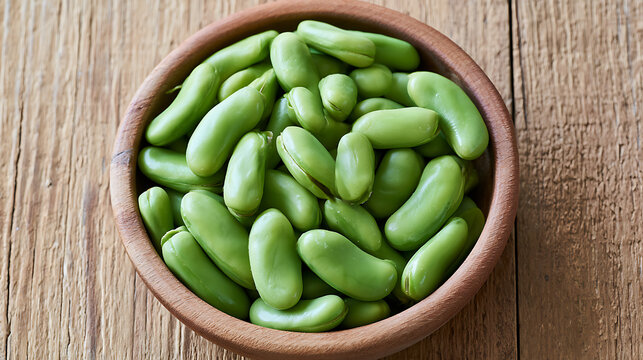 Fresh green fava beans or broad beans Vicia faba in a wooden bowl on a rustic wooden table, overhead view, healthy plant protein food