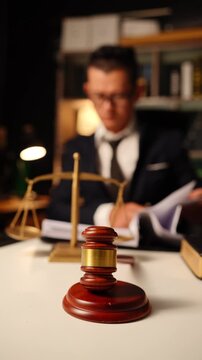 Brass scale of justice on desk with blurred lawyer holding hand on forehead in deep thought