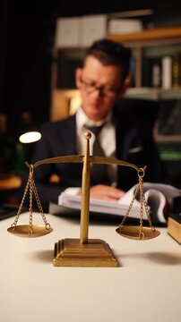 Brass scale of justice on desk with blurred lawyer holding hand on forehead in deep thought