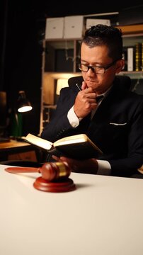 Lawyer reading and writing in law book sitting behind wooden judge gavel