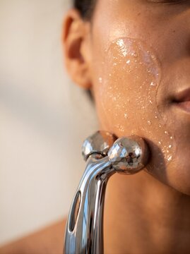Woman massaging her face with chrome dual-roller probe. Microcurrent facial massage, skincare and hardware cosmetology concept. Close-up shot for poster
