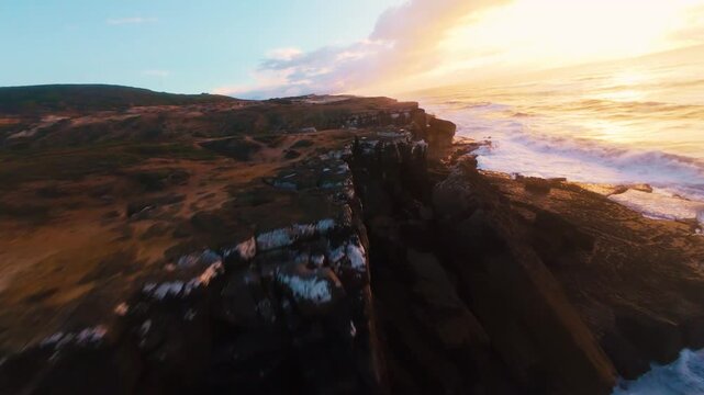 Sunset over rugged cliffs with crashing waves. Warm golden light reflects off ocean spray. Dramatic aerial view captures raw coastal beauty. Perfect for travel, nature, or adventure themes