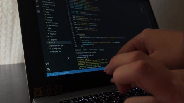 Woman programmer's hands typing on a laptop keyboard with coding language on the screen, female it specialist developing software application or website in the office